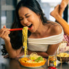 Woman eating noodles with chopsticks in a kitchen setting
