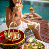 Woman enjoying a snack by a poolside with a package of SIAM spring roll wrappers on a table.